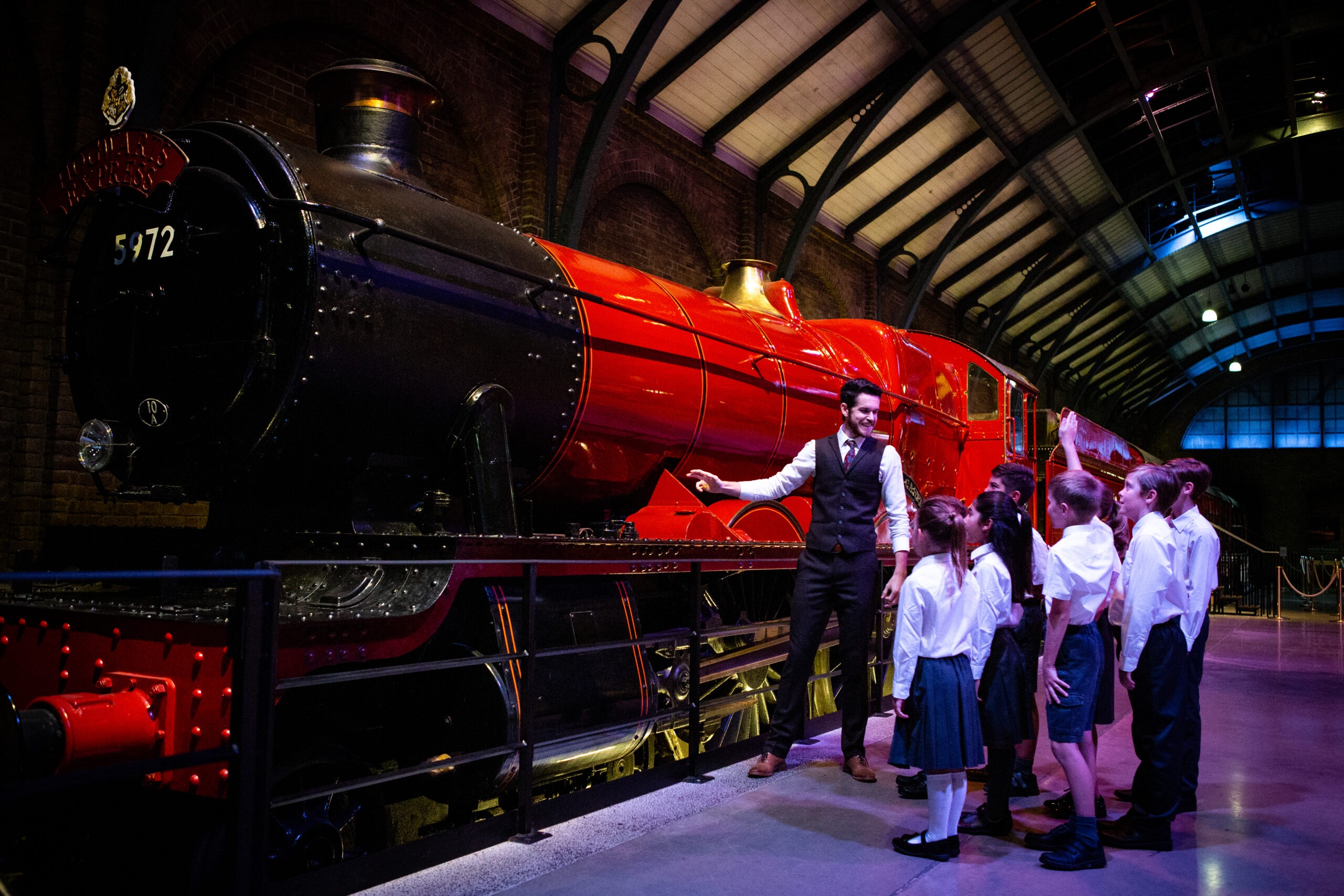 Teacher and group of school children in front of Hogwarts Express